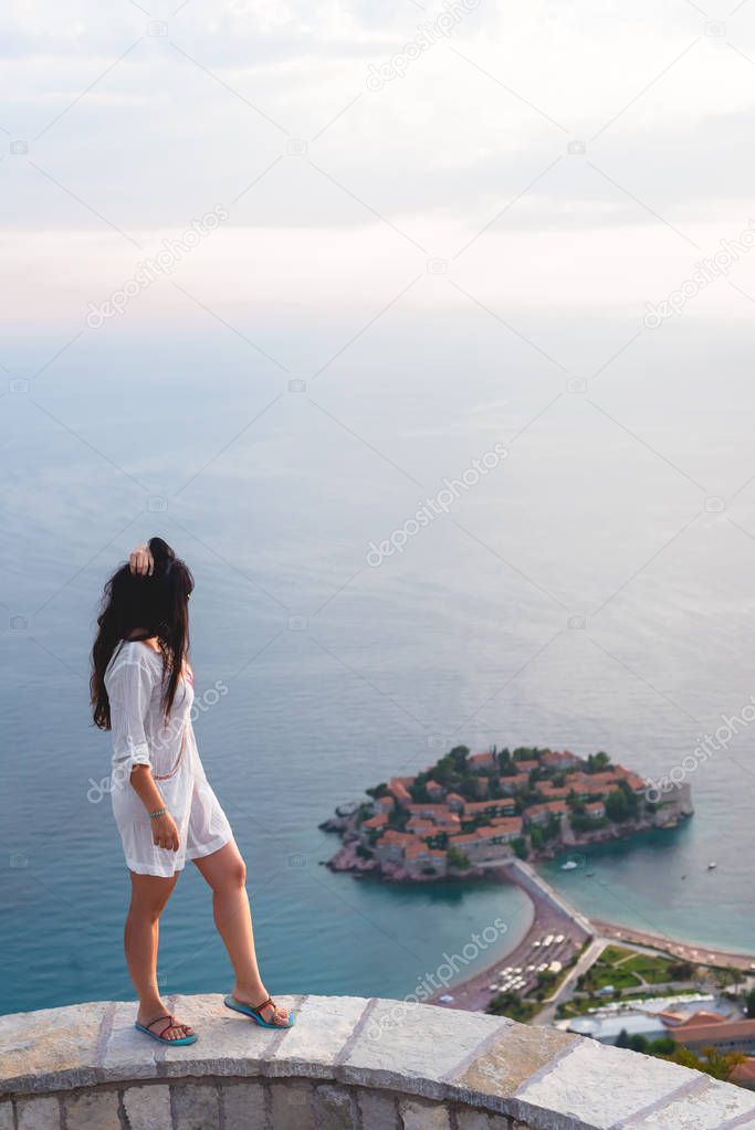 side view of woman looking at island of Sveti Stefan with hotel resort in Adriatic sea, Budva, Montenegro