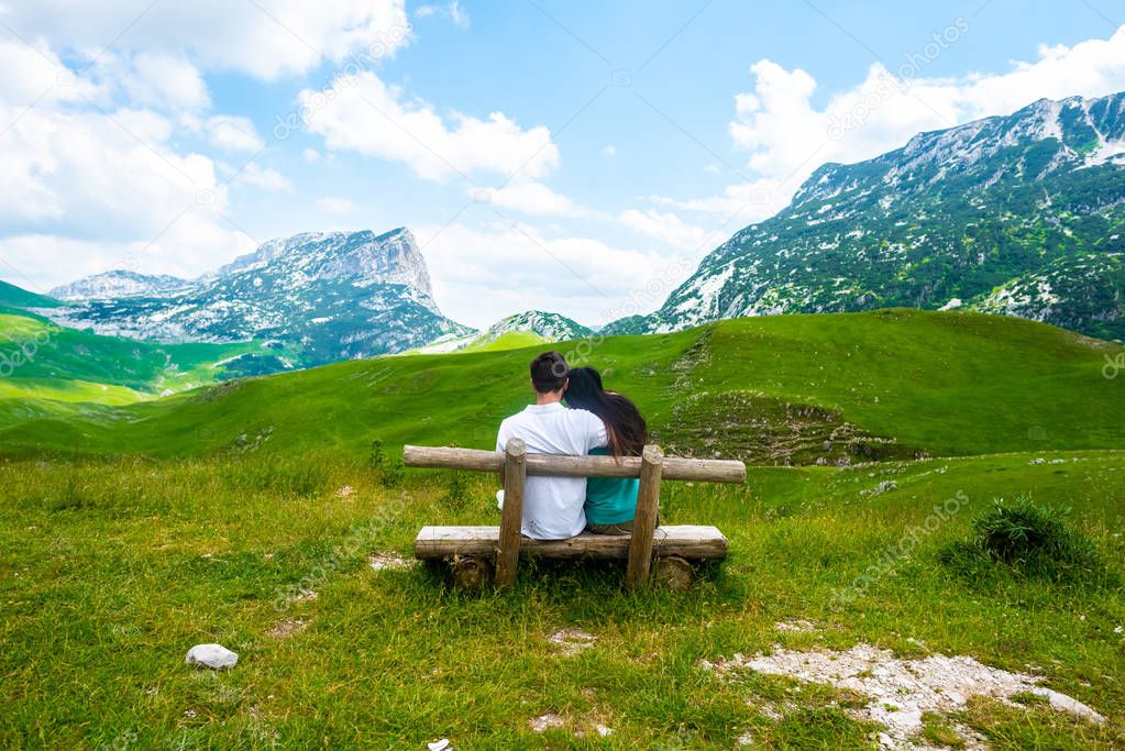 back view of couple sitting on wooden bench and looking at mountains in Durmitor massif, Montenegro