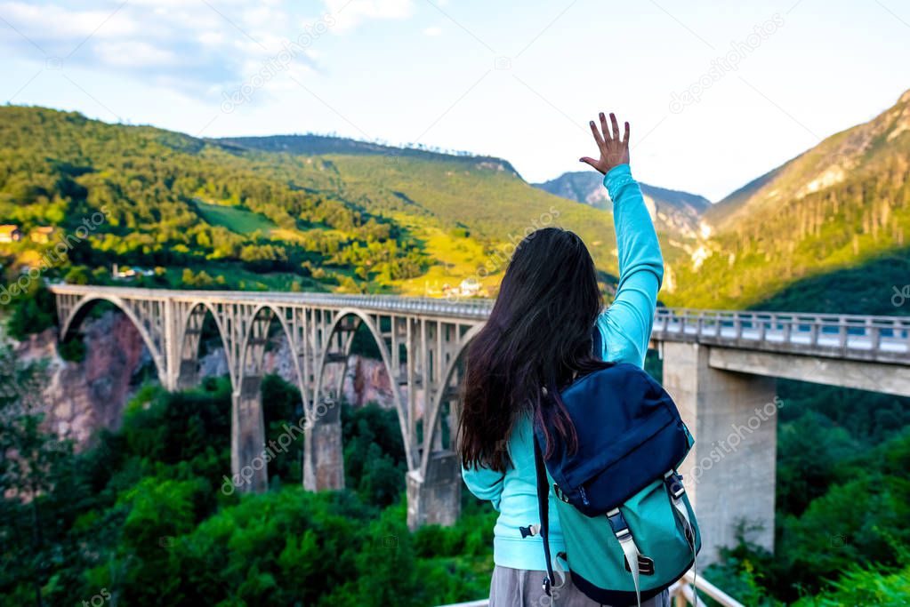 back view of woman waving hand to concrete arch bridge in Montenegro