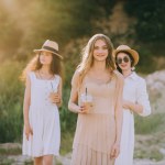 Attractive girls in straw hats holding coffee latte and walking in nature with sunlight