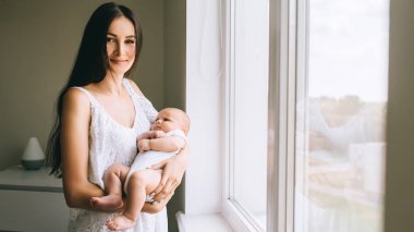 onun bebek evde pencere taşıma ve kameraya bakarak çekici genç anne