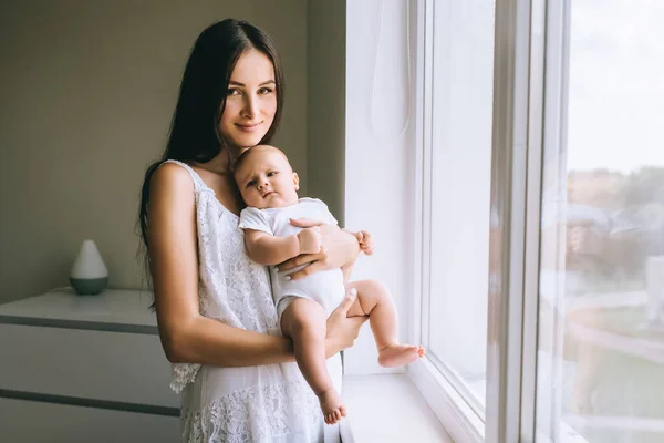 Onun Bebek Evde Pencere Taşıma Kameraya Bakarak Gülümseyen Genç Anne — Stok fotoğraf