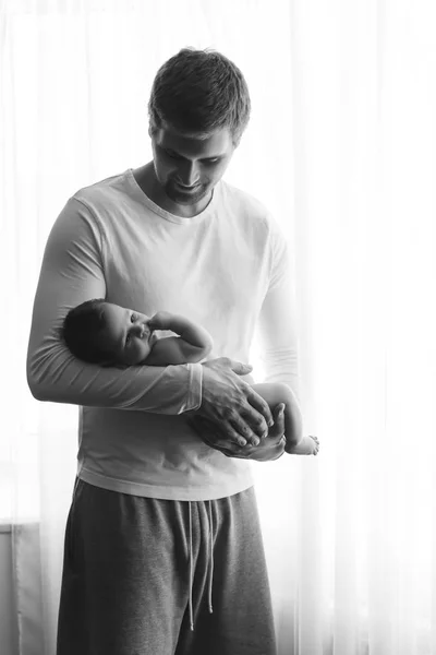 自宅のカーテンの前に小さな男の子を運ぶ父の黒と白の写真 — ストック写真