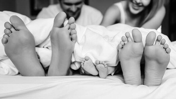 black and white picture of legs of family with infant son under blanket in bed at home
