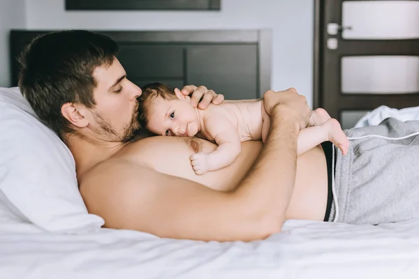 Vue Latérale Homme Torse Embrassant Bébé Garçon Dans Lit Maison Image En Vente