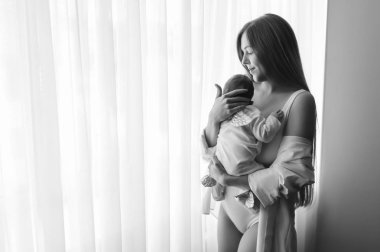 Anne küçük oğlu evde perdeler önünde taşıyan siyah beyaz resim