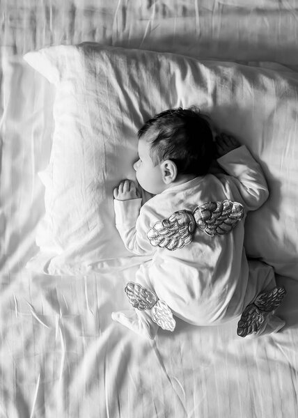 black and white picture of baby boy in costume with wings laying in bed at home