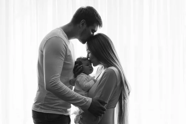 彼女は自宅のカーテンの前に彼らの男の子にキスしながら妻にキスをする男性の黒と白の写真 — ストック写真