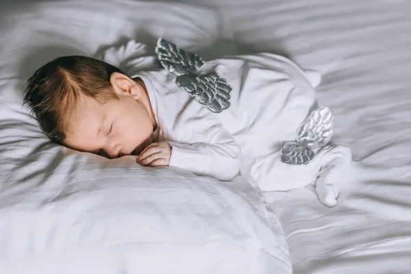 Suloinen Pieni Vauva Poika Puku Siivet Nukkuu Sängyssä Kotona tekijänoikeusvapaita kuvapankkikuvia
