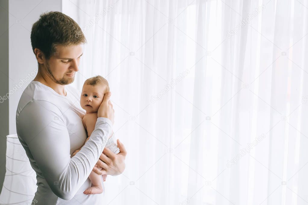 side view of father carrying little baby boy in front of curtains at home