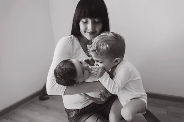 Black and white photo of mother with two little sons on hands at home — Stock Photo