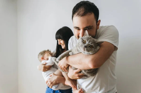 Retrato de padres felices sosteniendo al niño pequeño y al gato gris en casa - foto de stock