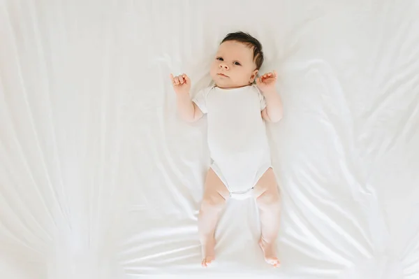 Overhead view of cute newborn baby in white bodysuit lying on bed — Stock Photo