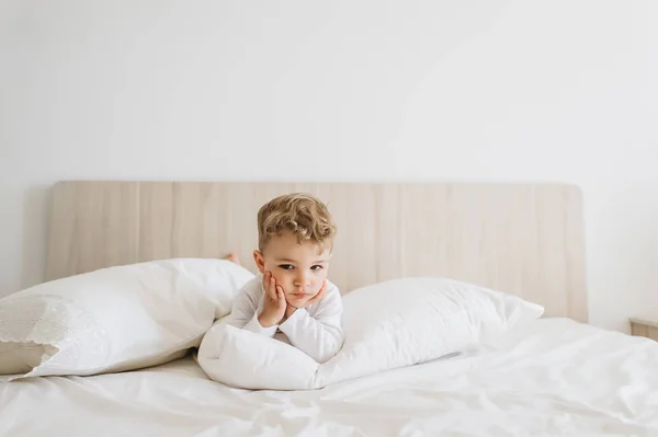 Очаровательный мальчик в белом купальнике лежит дома на кровати — стоковое фото