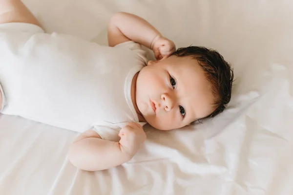 Крупним планом мила новонароджена дитина в білому боді костюмі лежить на ліжку — стокове фото