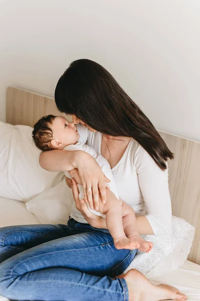 Portrait of mother holding little infant baby in hands while sitting on bed at home — Stock Photo