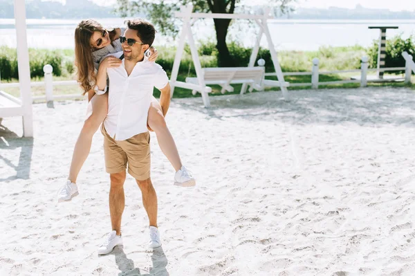 Sorrindo namorado dando piggyback para namorada na praia da cidade — Fotografia de Stock