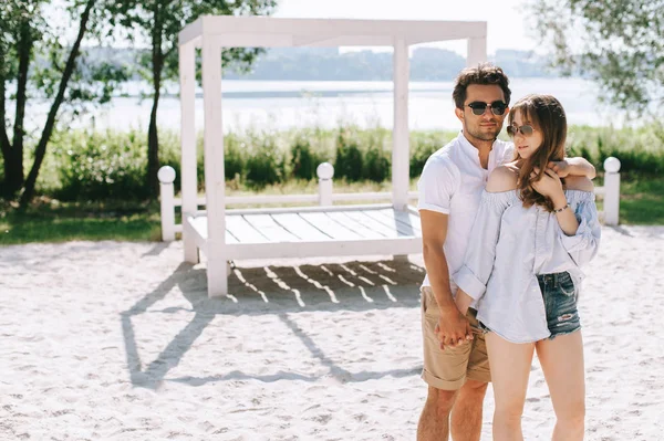 Novio feliz abrazando novia atractiva en la playa de arena de la ciudad - foto de stock