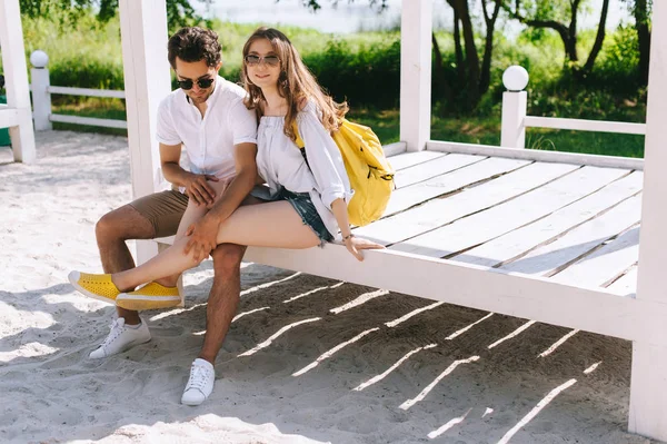 Young couple sitting on wooden bench at sandy city beach — Stock Photo