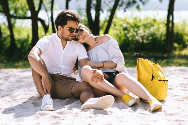 Affectionate couple hugging and sitting on sandy city beach — Stock Photo