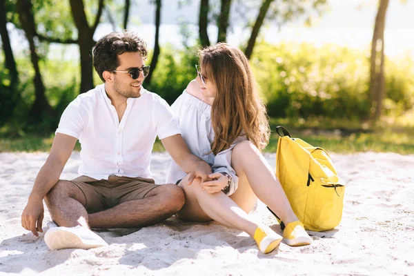 Happy couple sitting on sandy city beach and holding hands — Stock Photo