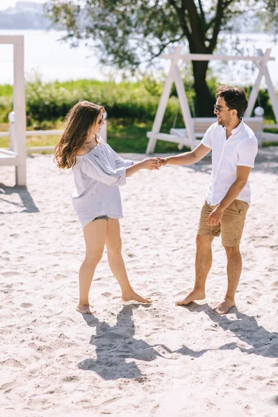 Casal de mãos dadas e olhando uns para os outros na praia da cidade arenosa — Fotografia de Stock