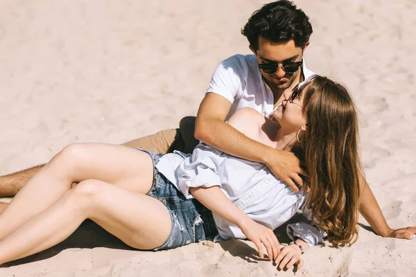 Улыбающаяся пара лежит на песчаном городском пляже и смотрит друг на друга — стоковое фото