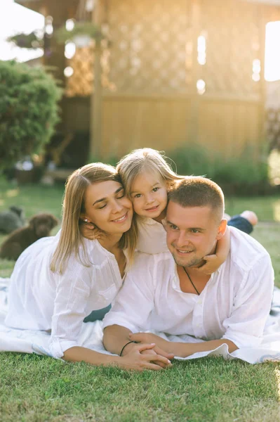 Portrait of smiling family with little daughter resting on cloth on ground together on backyard — Stock Photo
