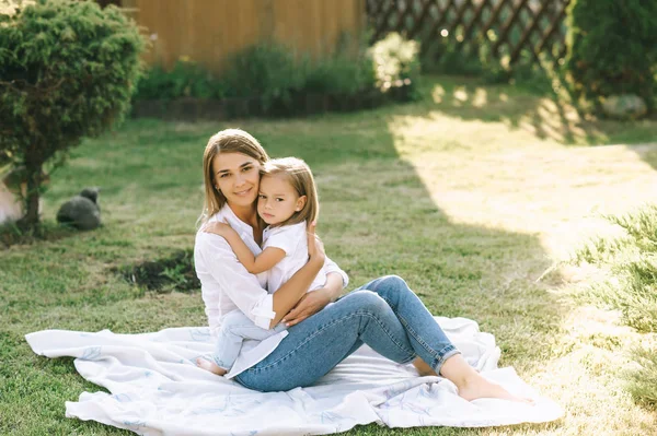 Glückliche Mutter und kleine Tochter umarmen einander, während sie gemeinsam auf einem Tuch im Hinterhof ruhen — Stockfoto