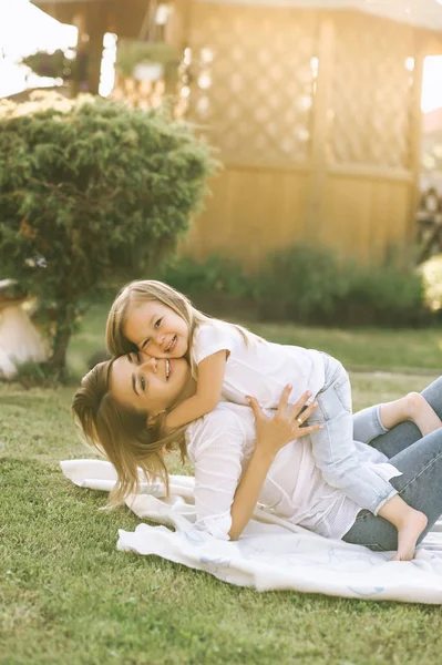 Счастливая мать и маленькая дочь обнимают друг друга, отдыхая на ткани вместе на заднем дворе — стоковое фото