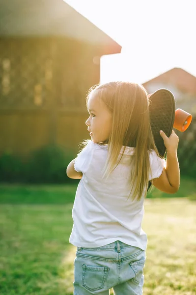 Back view of adorable little child holding skateboard in hands on yard — Stock Photo