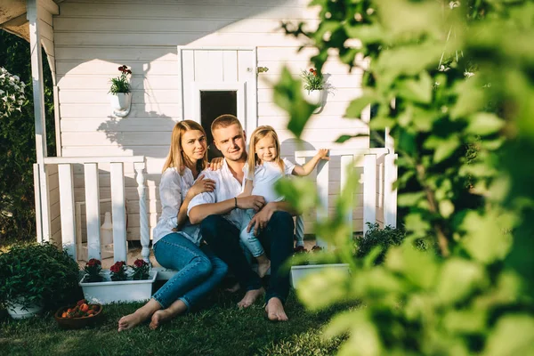 Famiglia sorridente con bambino piccolo seduto insieme sul portico di piccola casa di campagna — Foto stock