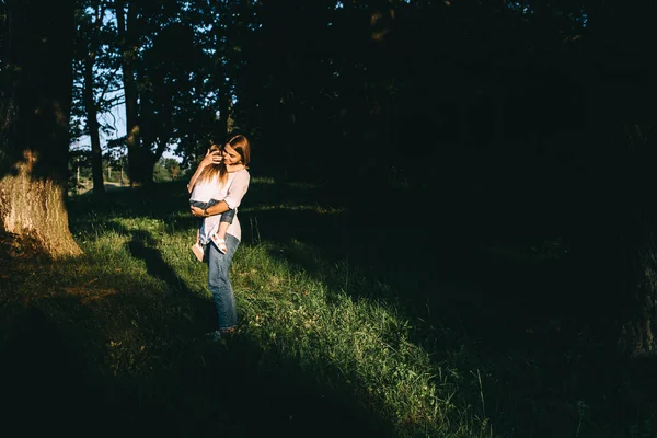 Vista lateral de la madre abrazando a la linda hija pequeña mientras está de pie en el bosque - foto de stock
