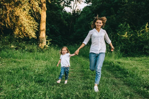 Junge Mutter und fröhliche Tochter halten sich Händchen, während sie gemeinsam im Wald laufen — Stockfoto