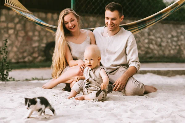 Heureux famille avec petit fils et chaton assis sur le sable avec hamac derrière à la campagne — Photo de stock