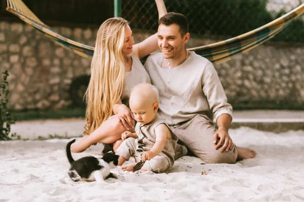 Família feliz com pequeno filho e gatinho sentado na areia no campo — Fotografia de Stock