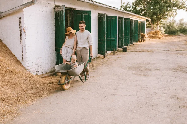 Padres e hijo pequeño en carretilla en el campo en el día de verano - foto de stock