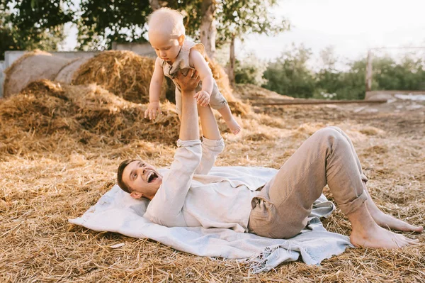Счастливый отец держит маленького сына, отдыхая на сене в деревне — стоковое фото