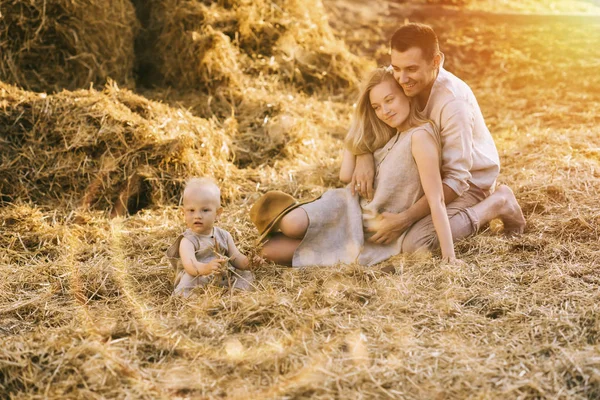 Parents and little son in linen clothing resting on hay at countryside — Stock Photo