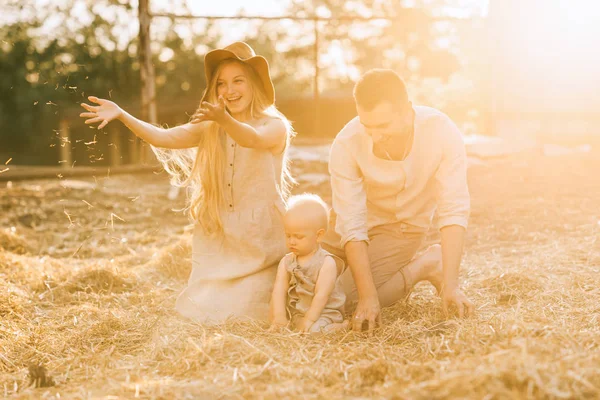 Glückliche Eltern und kleiner Sohn in Leinenkleidung, die auf dem Land auf Heu ruhen — Stockfoto