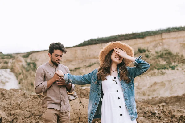 Stylish girl closing eyes and holding hands with happy boyfriend in sand canyon — Stock Photo