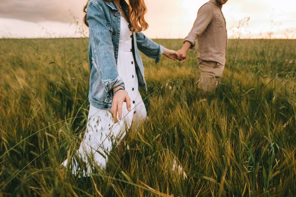 Cropped view of couple holding hands and walking on green summer meadow — Stock Photo