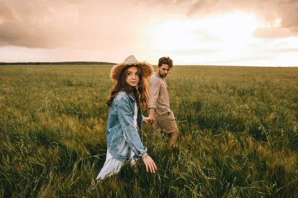 Atractiva pareja elegante cogida de la mano y caminando en el prado verde - foto de stock
