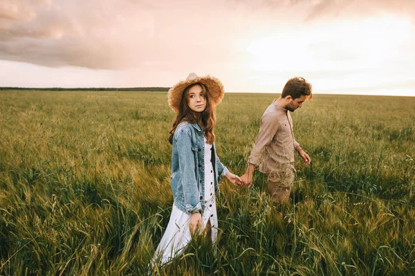 Молодая стильная пара, держась за руки и гуляя по зеленому лугу, история любви — стоковое фото