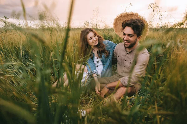 Glückliches stylisches Paar mit Strohhut sitzt im grünen Gras auf der Wiese — Stockfoto