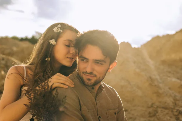 Beautiful tender girl with flowers in hair hugging her boyfriend in sand canyon — Stock Photo