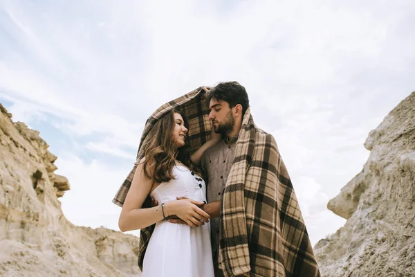 Casal feliz abraçando sob cobertor em desfiladeiro de areia com céu nublado — Fotografia de Stock