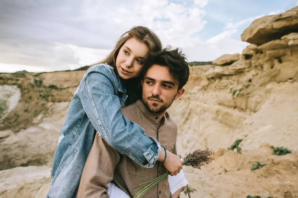Handsome boyfriend piggybacking his beautiful girlfriend in sand canyon — Stock Photo