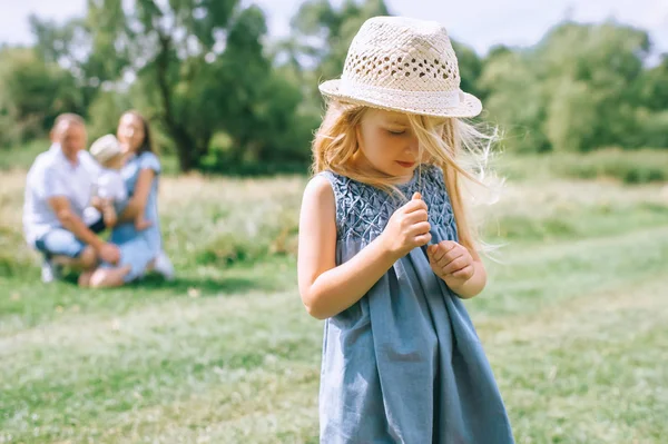 Adorable blonde girl in straw hat with family behind — Stock Photo