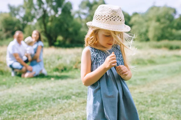 Adorable fille blonde en chapeau de paille avec la famille derrière — Photo de stock